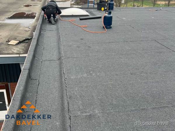 Dakdekker repareert bitumen dakbedekking op groot plat dak in Bavel